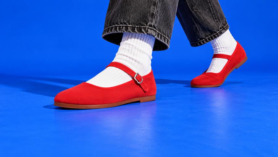 Red Easy USA Mary Janes with white ribbed socks and cropped charcoal jeans stepping across a cobalt-blue studio floor.